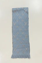 A light blue woven scarf with silver-tone embroidered monogram motifs and fringe at the bottom, laid flat on a white surface.