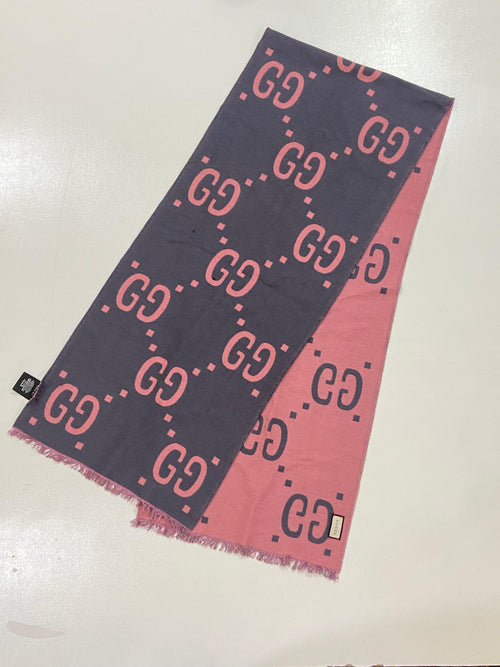 A Gucci scarf with a diagonal split design, featuring a dark navy blue side with pink GG monogram pattern and a pink side with dark navy monogram pattern, finished with fringed edges.