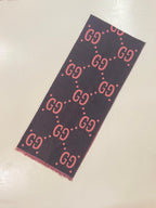 A dark charcoal gray scarf featuring a repeating pink and white Gucci GG monogram pattern, laid flat on a light beige surface.