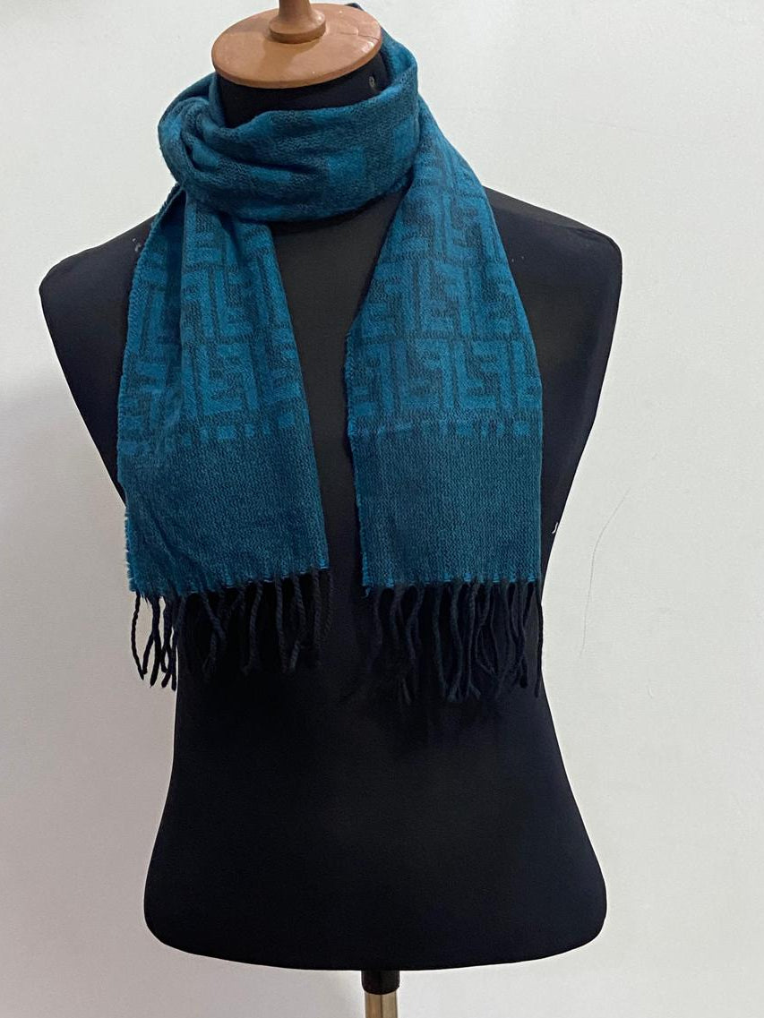 A teal blue patterned scarf with black fringe, displayed on a black mannequin torso against a plain white background.