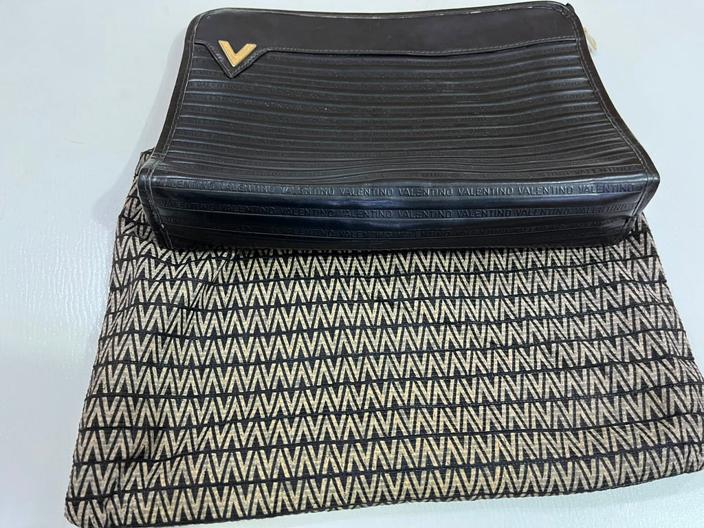 A black leather zip-around clutch with a small gold chevron logo, shown next to a black and beige patterned fabric pouch on a white background.