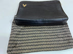A black leather zip-around clutch with a small gold chevron logo, shown next to a black and beige patterned fabric pouch on a white background.